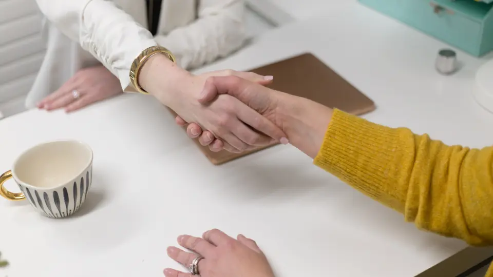 Two people shaking hands across a work desk