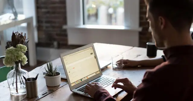 Man working on a laptop at a desk near a window