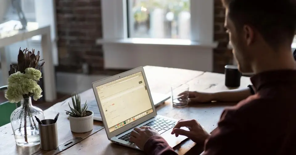 Man working on a laptop at a desk near a window