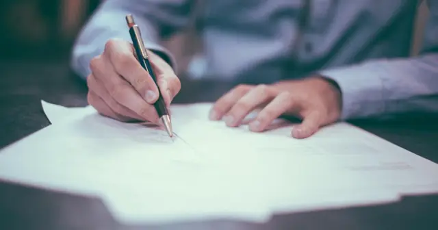 Hands writing with a pen on a sheet of paper