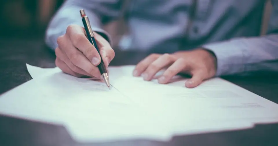 Hands writing with a pen on a sheet of paper