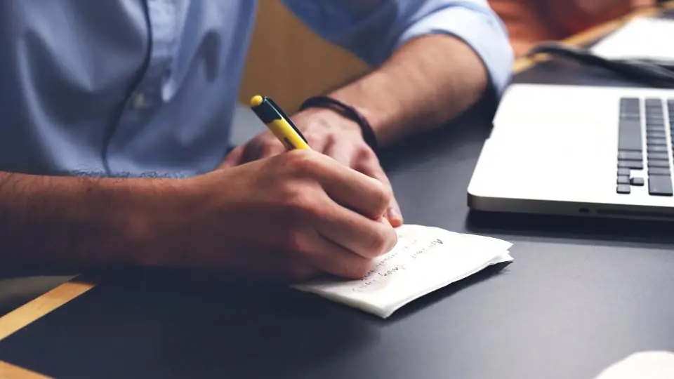 Man taking notes on a pad next to a laptop