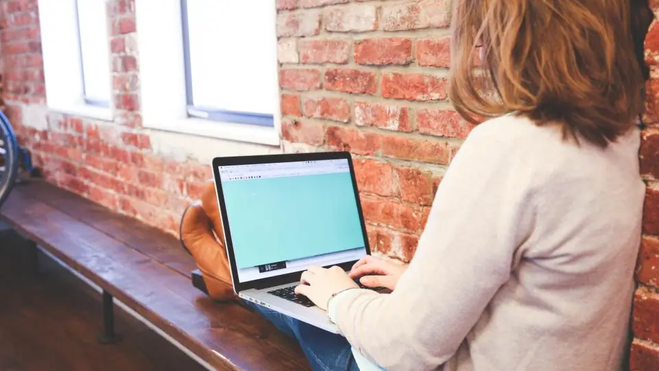 Woman working on a laptop next to a brick wall