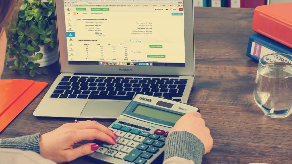 Hands using a calculator in front of a laptop with a spreadsheet open