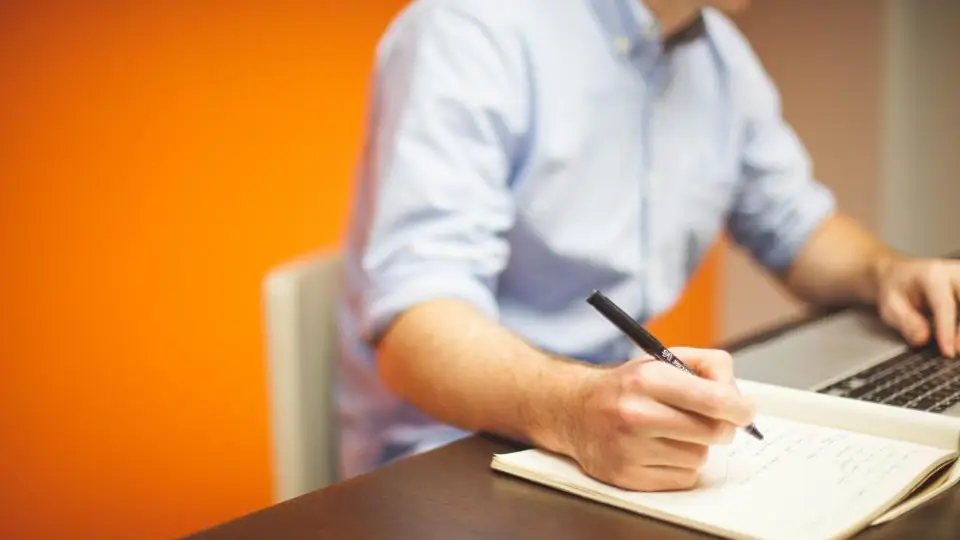 Man writing in a notebook next to a laptop